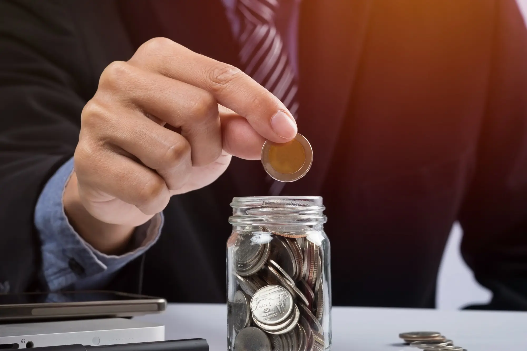 Hand placing a coin into a jar filled with various coins.