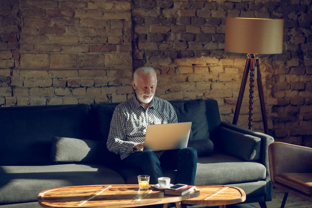 Elderly man using laptop on sofa